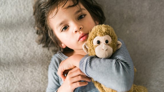 How to care for toddler coughs, sick toddler boy lying down holding stuffed monkey